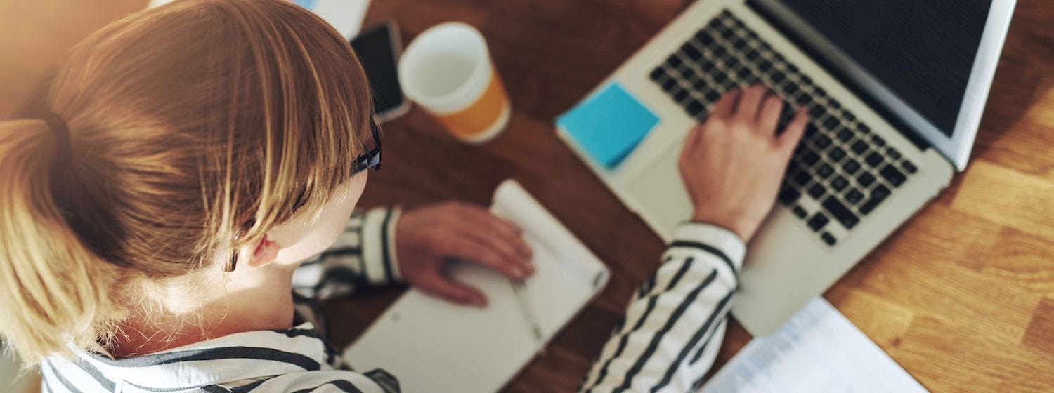 Stay motivated- Young Woman working on laptop with notepad and pen